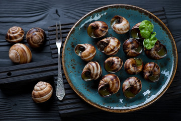 Baked snails with garlic herbs butter on a black serving board