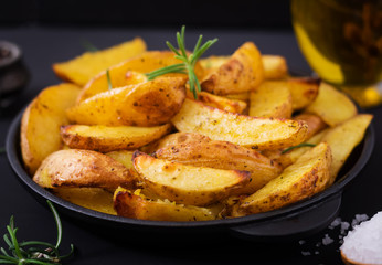 Ruddy Baked potato wedges with rosemary and garlic on a dark background.
