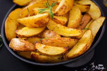 Ruddy Baked potato wedges with rosemary and garlic on a dark background.