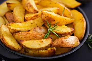 Ruddy Baked potato wedges with rosemary and garlic on a dark background.