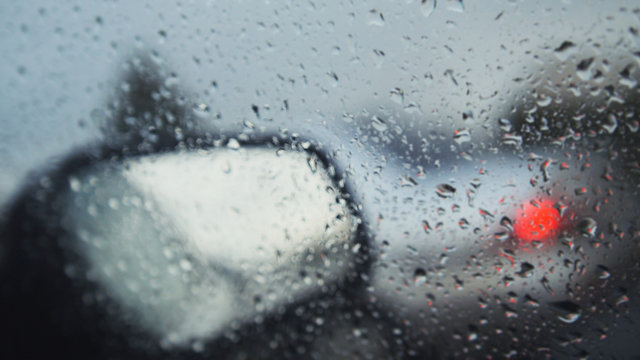 Car glass on a rainy day - defocused background. Moving waterdrops in the wipers of the windshield