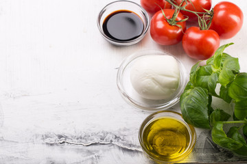 Ingredients for cooking italian capreze salad cherry tomatoes, basil leaves, mozzarella cheese, spices and olive oil on wooden rustic background top view close up