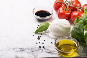 Ingredients for cooking italian capreze salad cherry tomatoes, basil leaves, mozzarella cheese, spices and olive oil on wooden rustic background top view close up