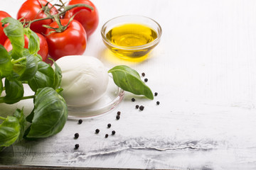 Ingredients for cooking italian capreze salad cherry tomatoes, basil leaves, mozzarella cheese, spices and olive oil on wooden rustic background top view close up