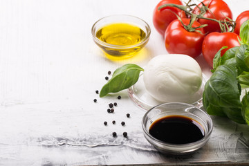 Ingredients for cooking italian capreze salad cherry tomatoes, basil leaves, mozzarella cheese, spices and olive oil on wooden rustic background top view close up