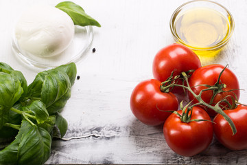 Ingredients for cooking italian capreze salad cherry tomatoes, basilic, mozzarella cheese, spices and olive oil on wooden rustic background top view close up