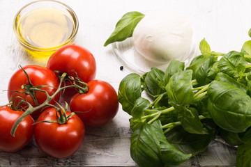 Ingredients for cooking italian capreze salad cherry tomatoes, basil leaves, mozzarella cheese, spices and olive oil on wooden rustic background top view close up