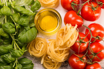 Italian food background with vine tomatoes, basil, tagliatelle pasta on white background Top view
