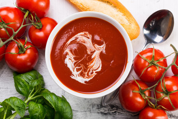 Tomato soup with basilic, cherry tomatoes and baguette on white background Top view