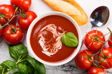 Tomato soup with basilic, cherry tomatoes and baguette on white background Top view