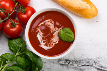 Tomato soup with basilic, cherry tomatoes and baguette on white background Top view
