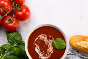 Tomato soup with basilic, cherry tomatoes and baguette on white background Top view