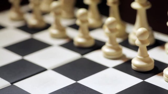 Panning shot of a chess board, with a hand moving the white pawn.