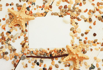 
Beach-themed empty paper note framed with sea pebbles, stars, driftwood decor, top view. Soft light and focus.