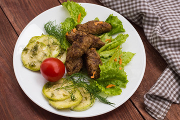 Meat dish called fingers with greens. Wooden table. Close-up