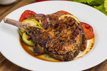 Pork steak on the bone grilled with vegetables. Wooden background. Top view. Close-up