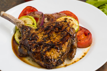 Pork steak on the bone grilled with vegetables. Wooden background. Top view. Close-up