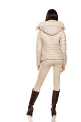 back view of a young woman in a winter jacket and boots posing on a white background