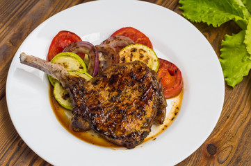 Pork steak on the bone grilled with vegetables. Wooden background. Top view. Close-up