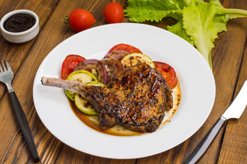 Pork steak on the bone grilled with vegetables. Wooden background. Top view. Close-up