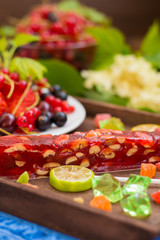 Churchkhela Georgian national delicacy, with different sweets and berries on a background of flowers. Wooden table. Close-up
