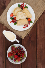 Dumplings with strawberries on a background of wild berries. Wooden rustic table. Top view. Close-up