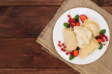 Dumplings with strawberries on a background of wild berries. Wooden rustic table. Top view. Close-up