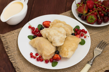 Dumplings with strawberries on a background of wild berries. Wooden rustic table. Close-up