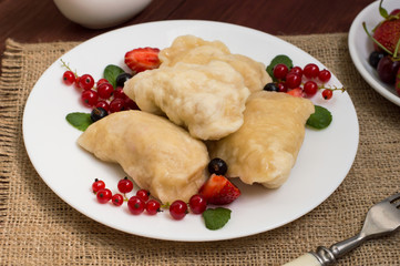 Dumplings with strawberries on a background of wild berries. Wooden rustic table. Close-up