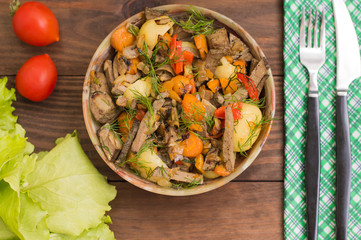 Braised liver with onions, carrots, potatoes and spices on stone plate. Wooden background. Top view. Close-up