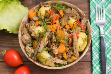 Braised liver with onions, carrots, potatoes and spices on stone plate. Wooden background. Top view. Close-up