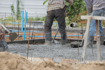 Concrete casting work.Worker wearing blue jeans and plastic brown boots leveling concrete work step of the building construction.