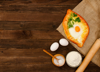 Khachapuri with eggs on sackcloth, salt, flour, eggs and parsley on the wooden table, space for text