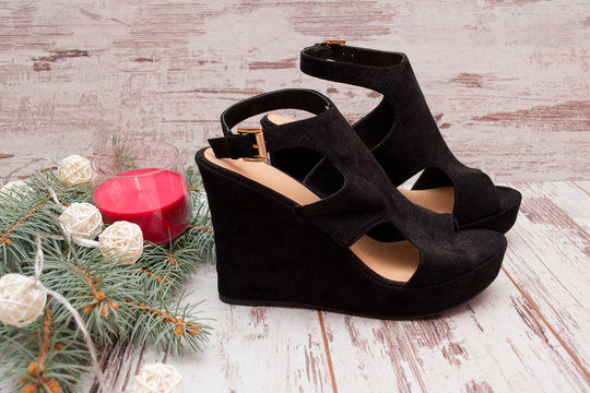 Black suede shoes on a wooden background, fir branch, garland and candle. fashion concept