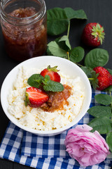 Cottage cheese and jam of roses with a strawberry. Wooden black table. Top view. Close-up