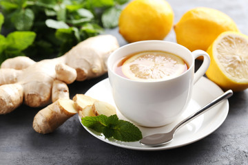 Cup of tea with ginger root and lemon on grey wooden table