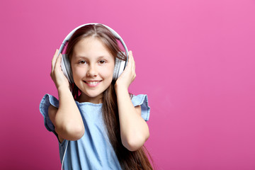 Portrait of young girl with headphones on pink background