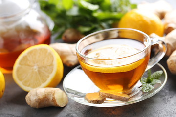 Cup of tea with ginger root and lemon on grey wooden table