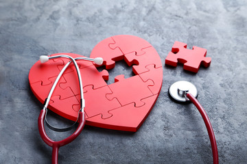 Red puzzle heart with stethoscope on grey wooden background