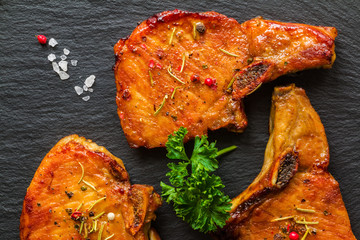 Roasted pork steaks, cutlets with bones  and fresh parsley on black stone background, top view.