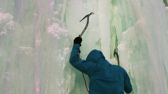 Young man with ice axes and crampons training to climb on icefall
