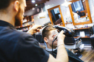 Male barber makes hair styling using a dryer.