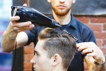 Male barber makes hair styling using a dryer.