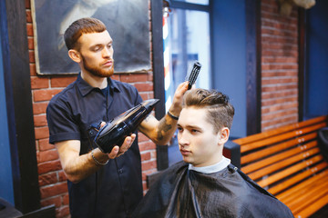 Male barber makes hair styling using a dryer.