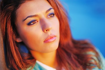 Naklejka premium Portrait of young beautiful pensive girl with brown hair in the bright rays of sunset on blurred background, close up.