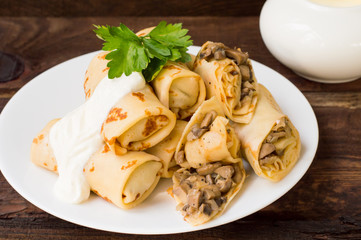 Pancakes stuffed with mushrooms and sour cream on a rustic wooden table. Top view. Close-up