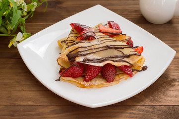 Pancakes with strawberries, topped  chocolate. Wooden table. Top view