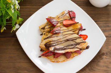 Pancakes with strawberries, topped  chocolate. Wooden table. Top view