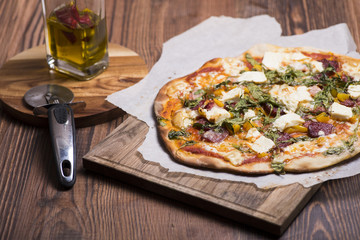 House made pizza salami with prosciutto, cheese, rucola, tomato sauce and yellow pepper on a wooden table