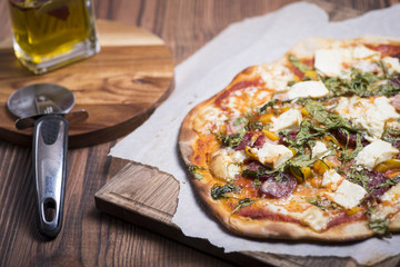 House made pizza salami with prosciutto, cheese, rucola, tomato sauce and yellow pepper on a wooden table
